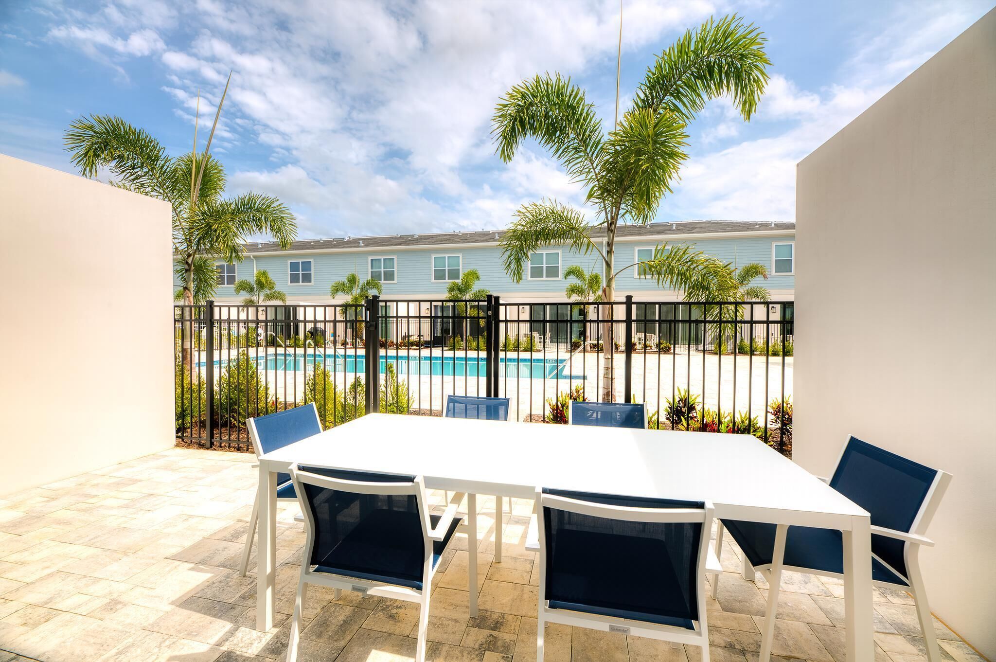 Un patio con una mesa y sillas blancas, una piscina y una hilera de palmeras.