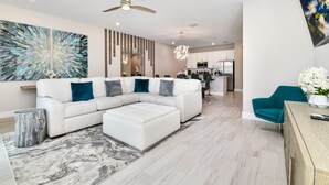 A modern living room with a sectional sofa, a coffee table, and a dining area with a teal chair.