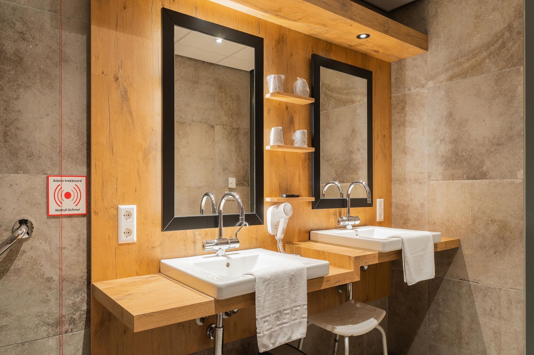 A modern bathroom with wooden accents, two sinks, a hairdryer, and a mirror.
