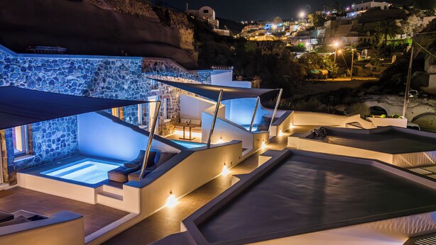 A modern resort with outdoor hot tubs, stone walls, and a view of the hillside. - Victoria Caves (Santorini)