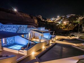 A modern resort with outdoor hot tubs, stone walls, and a view of the hillside. - Victoria Caves (Santorini)
