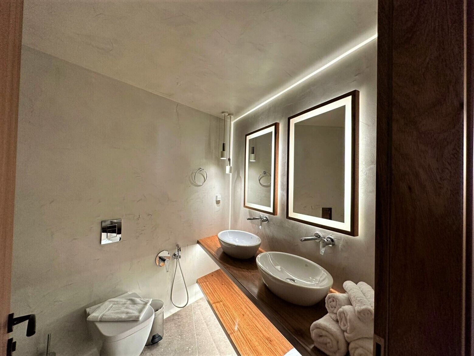 A modern bathroom with a wooden vanity, two sinks, and a toilet.