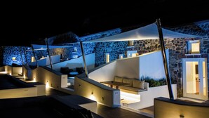 A modern outdoor lounge area with stone walls and built-in seating, illuminated by ambient lighting. - Victoria Caves (Santorini)