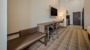 Une chambre d’hôtel comprenant un lit, un bureau avec une chaise, un banc, un téléviseur fixé au mur et une porte donnant accès à une salle de bain.