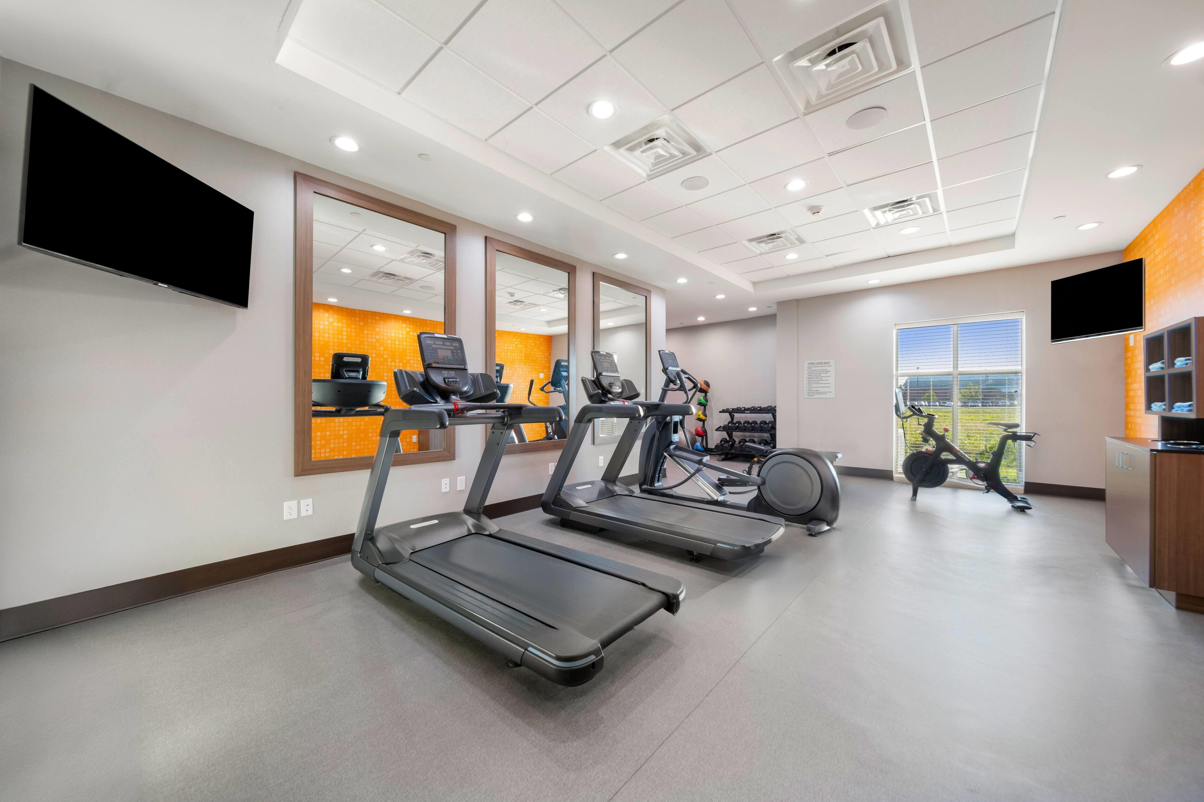 A gym with treadmills, exercise bikes, and a television screen.