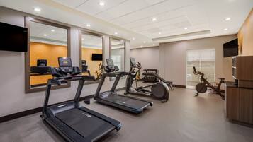 A gym with treadmills, stationary bikes, and a TV screen.