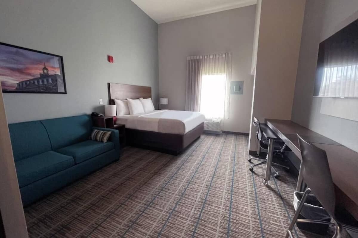 Ein Hotelzimmer mit Bett, Schreibtisch, Sofa und einem Gemälde an der Wand.
