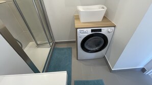 A compact laundry area with a washing machine, a drying rack, and a shower.