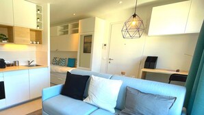A modern living space with a light blue sofa, a kitchen area with white cabinets, and a dining area with a table and chairs.