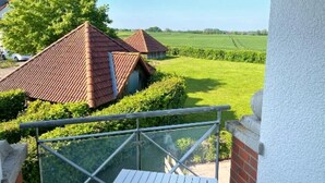 Il s’agit d’une propriété résidentielle dotée d’un balcon donnant sur un champ verdoyant et sur la maison voisine.