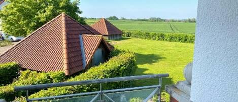 A residential property with a balcony overlooking a green field and a neighboring house.