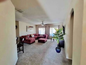 Relax in this spacious living room with a large L-shaped sofa, ceiling fan, and a beautiful potted plant.