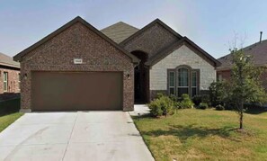 Stunning home with a brick garage door and symmetrical design, set amidst a beautifully manicured lawn and lush greenery.