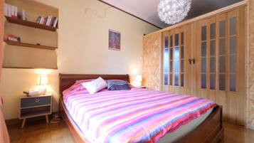 Une chambre à coucher avec un grand lit, une armoire en bois, des tables de chevet et un luminaire fixé au plafond.