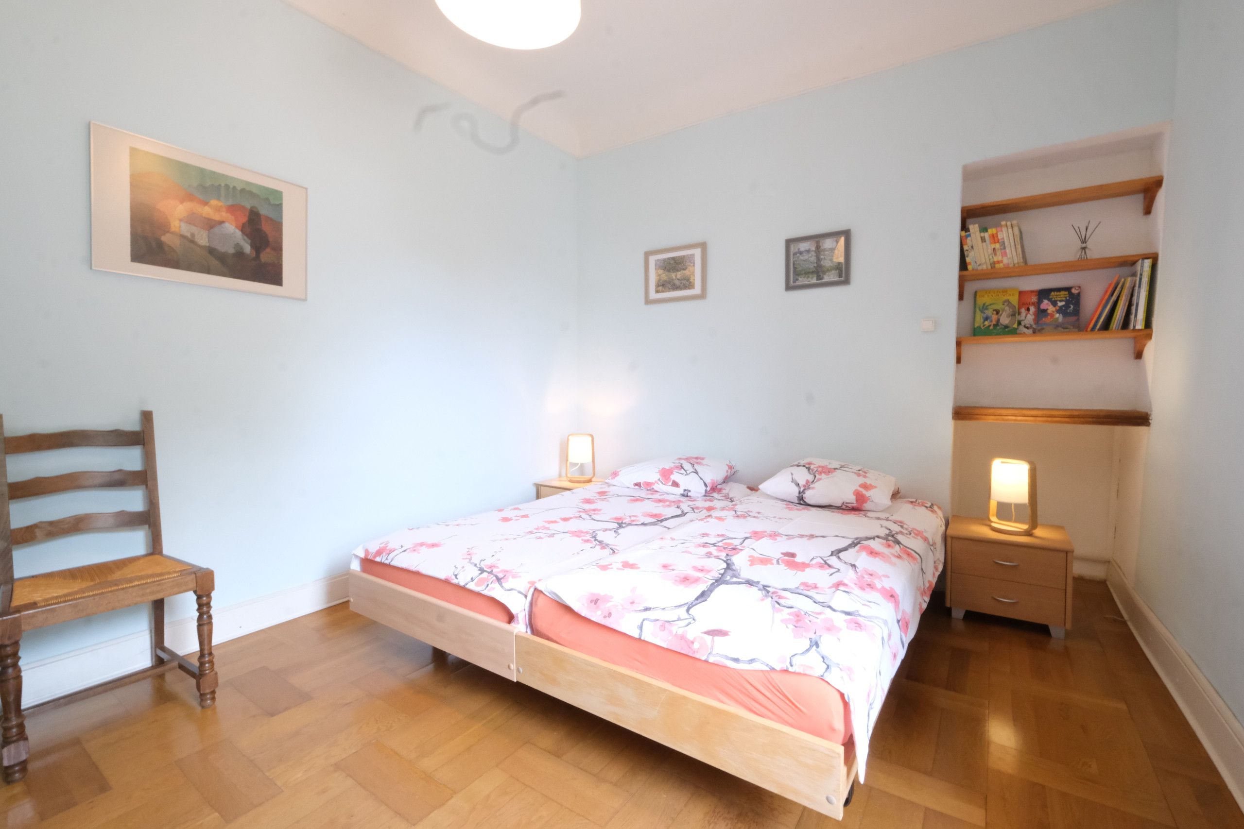 A bedroom with a bed, a chair, bedside tables, and a bookshelf.