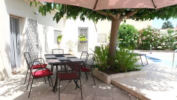 Une terrasse extérieure avec une table et des chaises, un arbre et une piscine en arrière-plan.