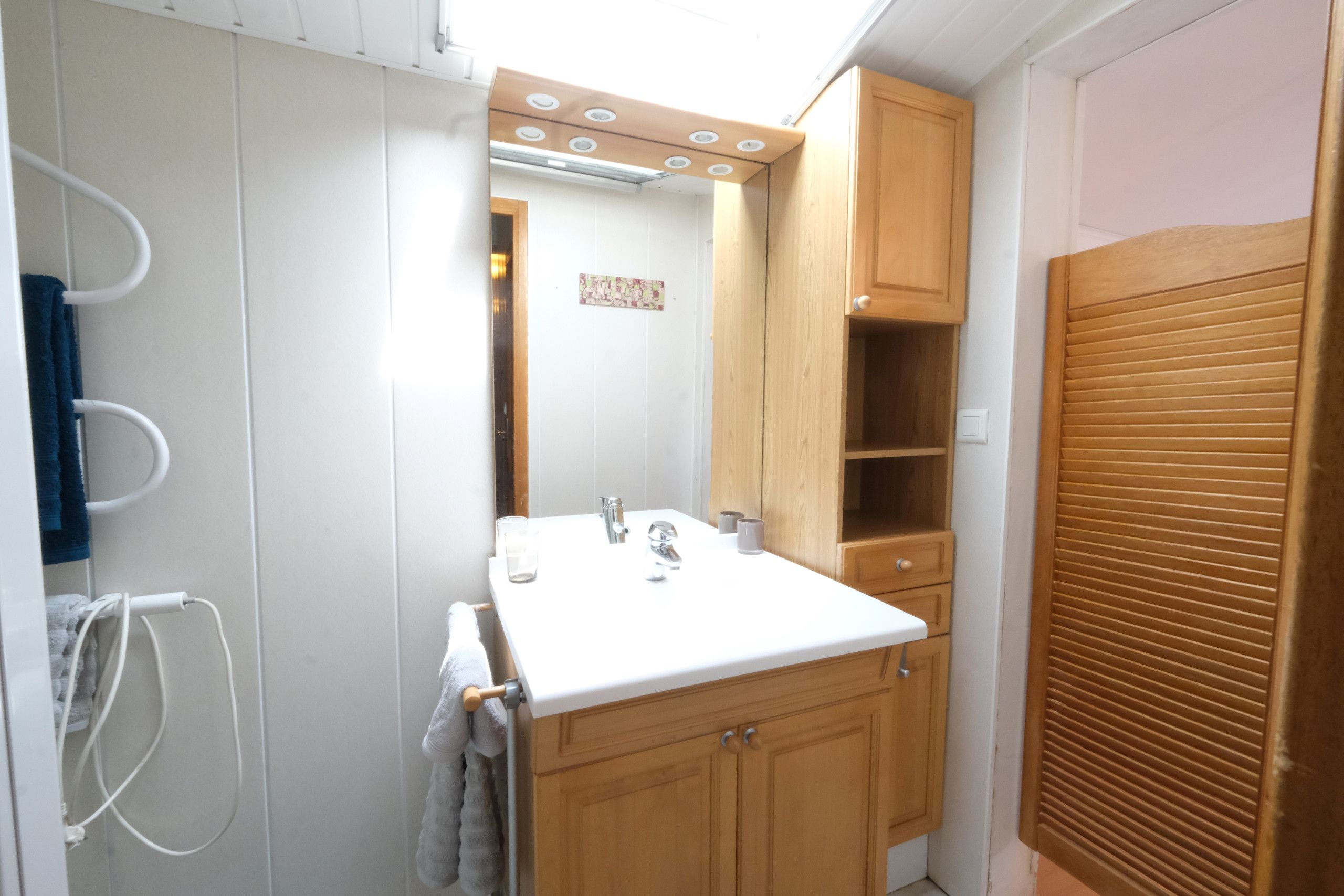 A compact bathroom with a white sink, wooden cabinets, and a towel rack.