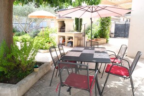 An outdoor patio with a table and chairs, a grill, and potted plants.