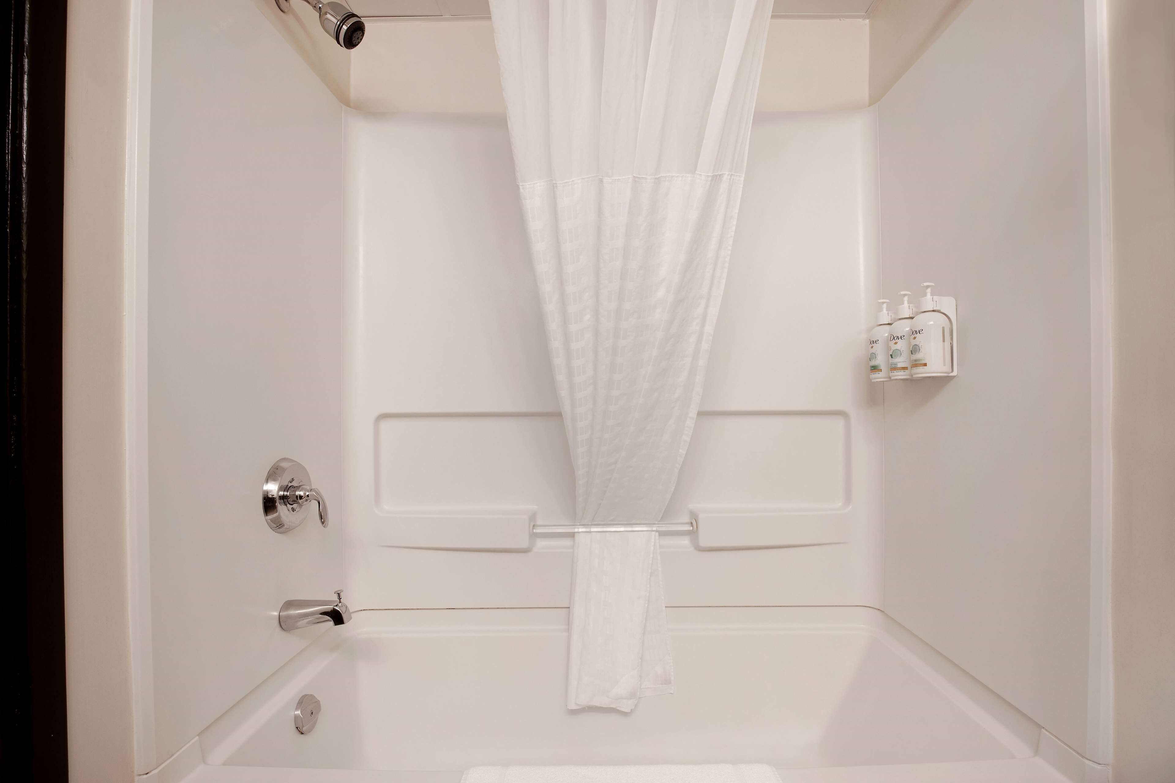 Un baño blanco con cortina de ducha, un perchero y una botella de jabón para manos.