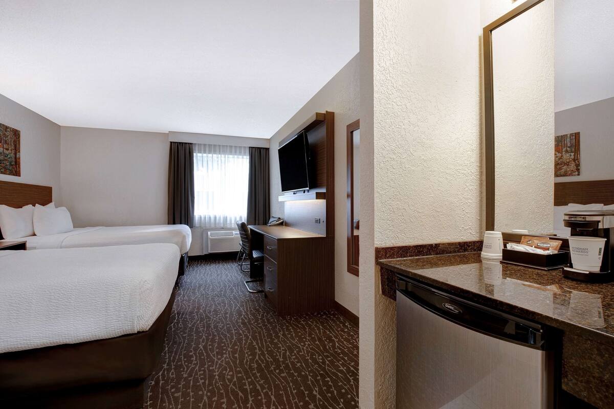 Ein Hotelzimmer mit zwei Betten, einem Schreibtisch, einem Fernseher, einer Kaffeemaschine und einem großen Spiegel.