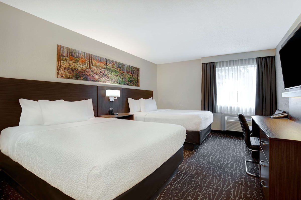 Ein Hotelzimmer mit zwei Betten, einem Schreibtisch, einem Sessel, einem Fernseher und einem Bild an der Wand.
