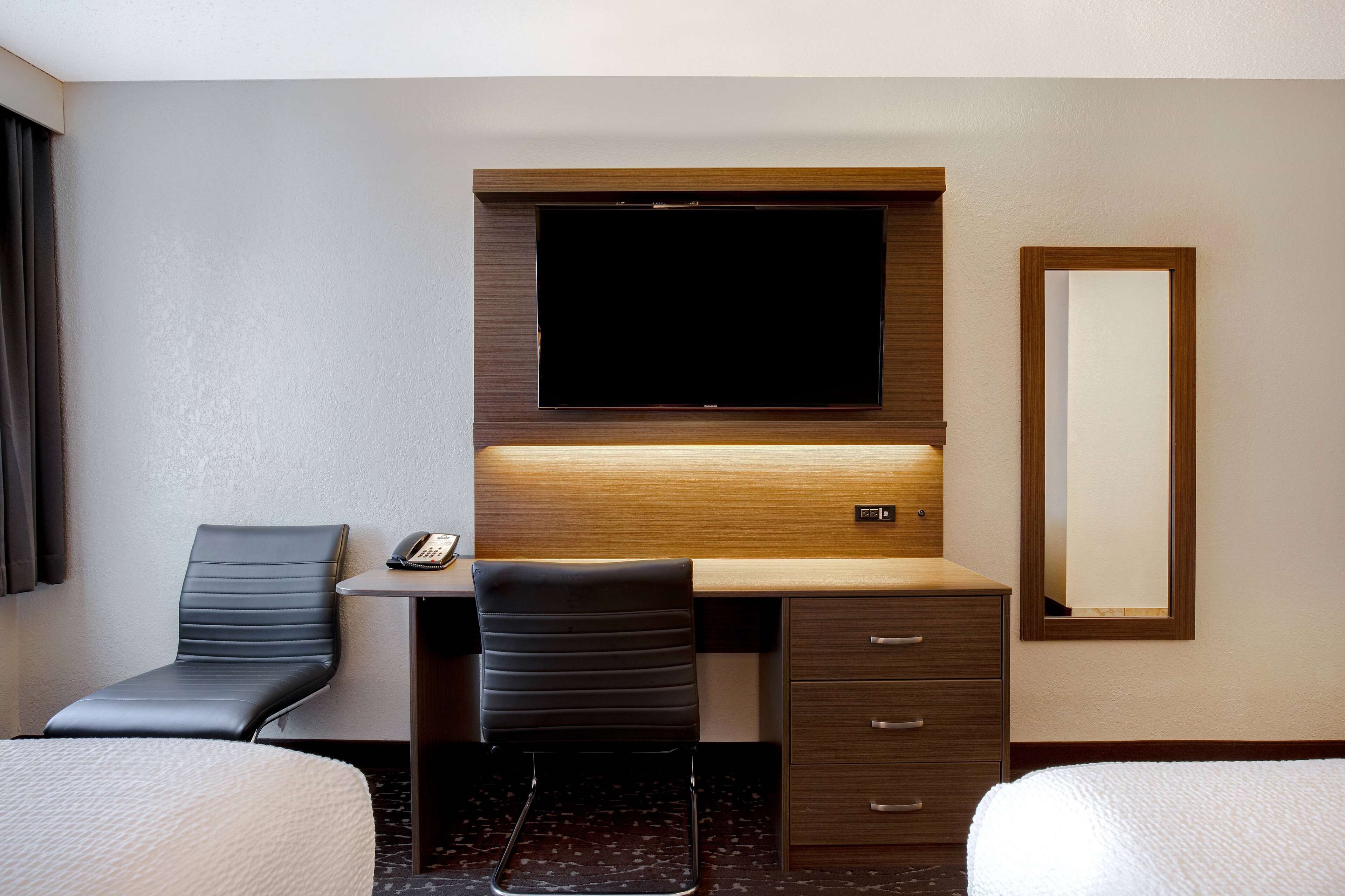 Habitación de hotel con cama, escritorio con silla, televisor de pantalla plana, espejo y teléfono.