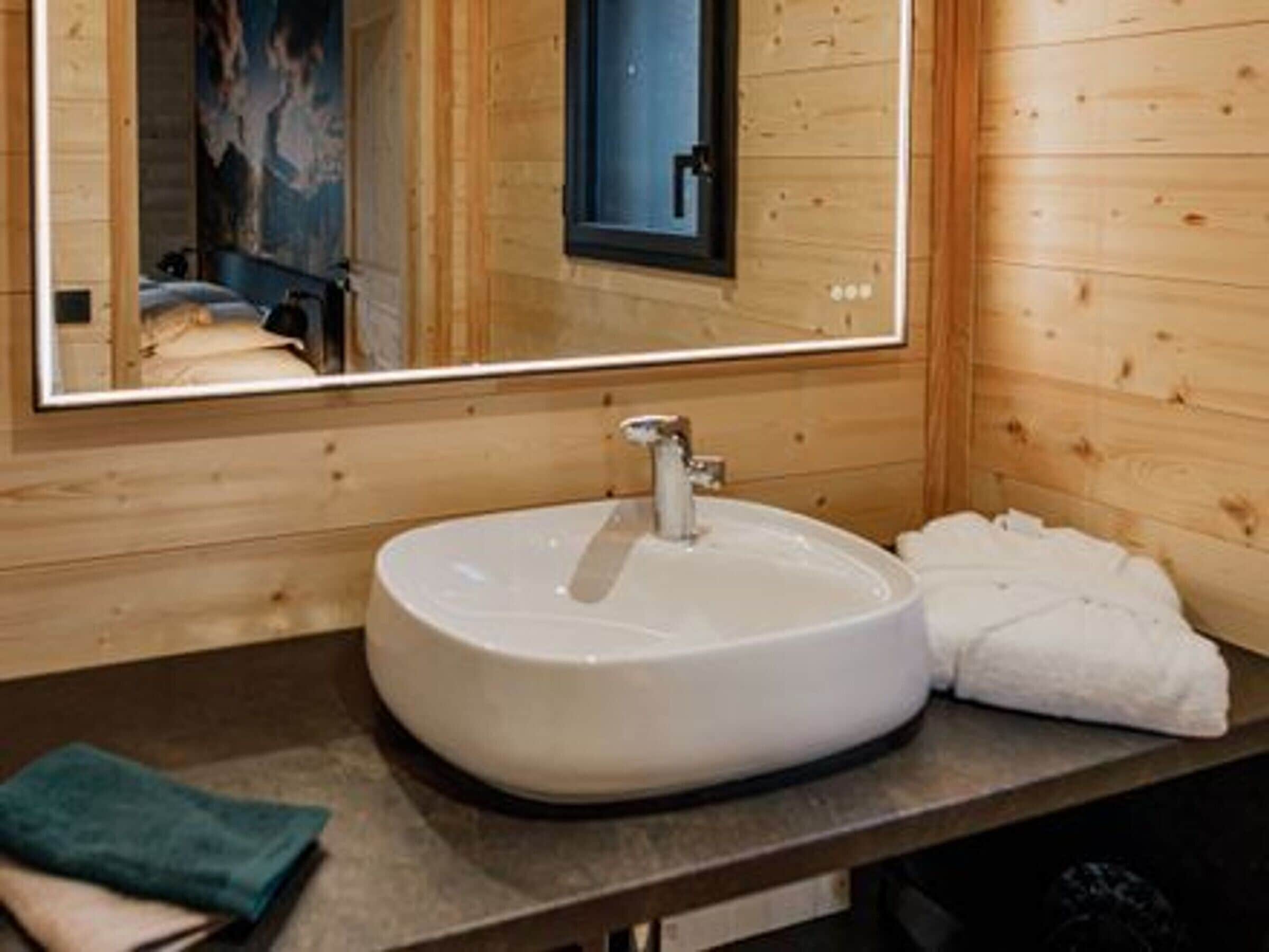 A wooden cabin interior with a round white sink, a mirror, and a towel on the counter.