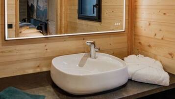 A wooden cabin interior with a round white sink, a mirror, and a towel on the counter.