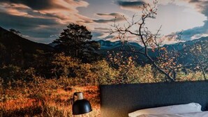 A bedroom with a bed, a lamp, and a view of a mountainous landscape.