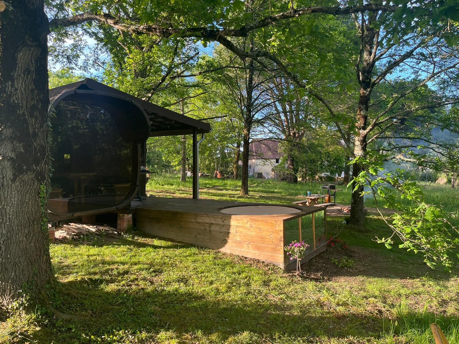 Una terraza de madera con una parrilla, rodeada de árboles y un césped.