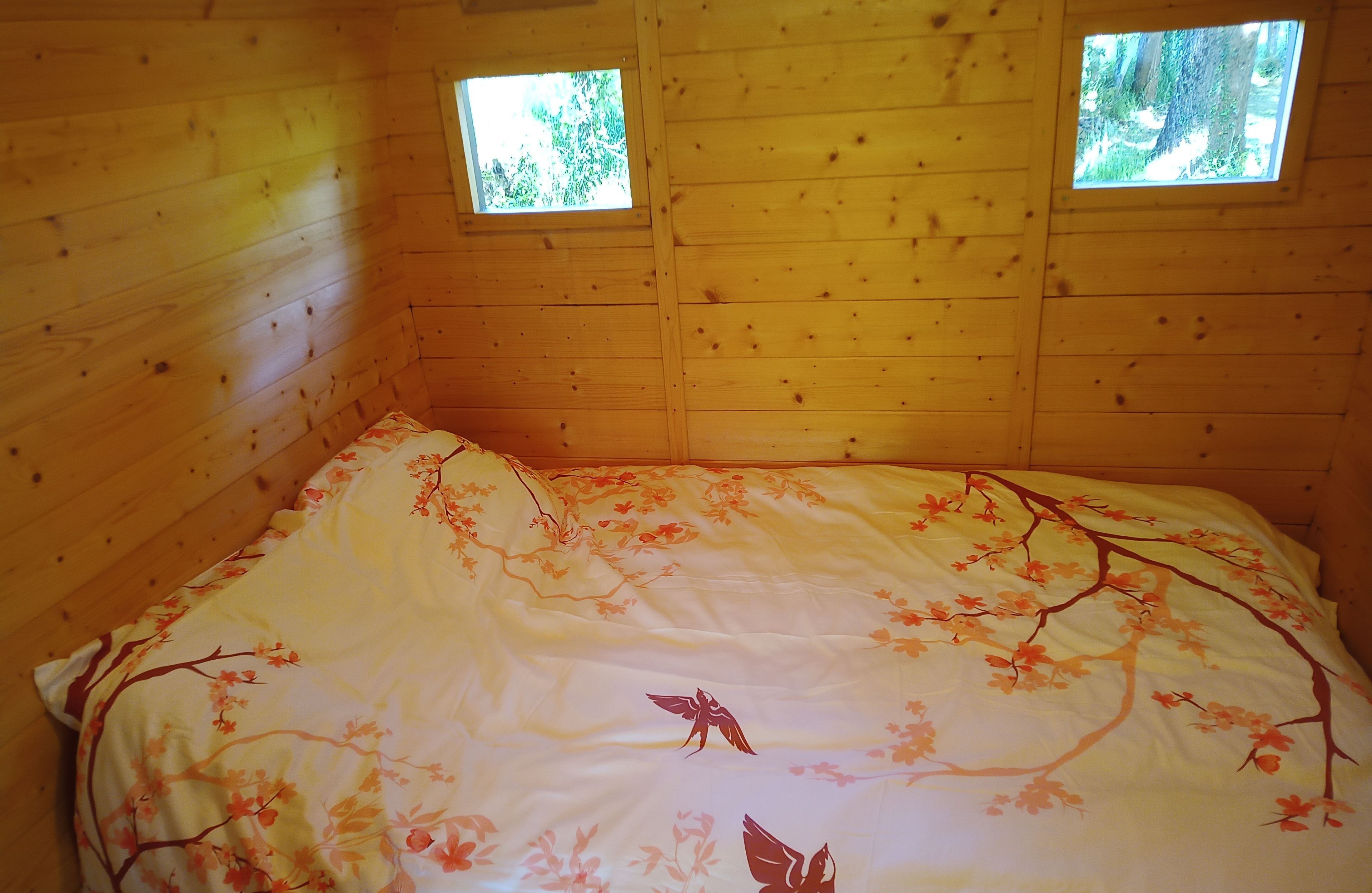 Een houten kamer met een bed, twee kleine ramen en een bloemenbedekking.