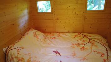 Een houten kamer met een bed, twee kleine ramen en een bloemenbedekking.