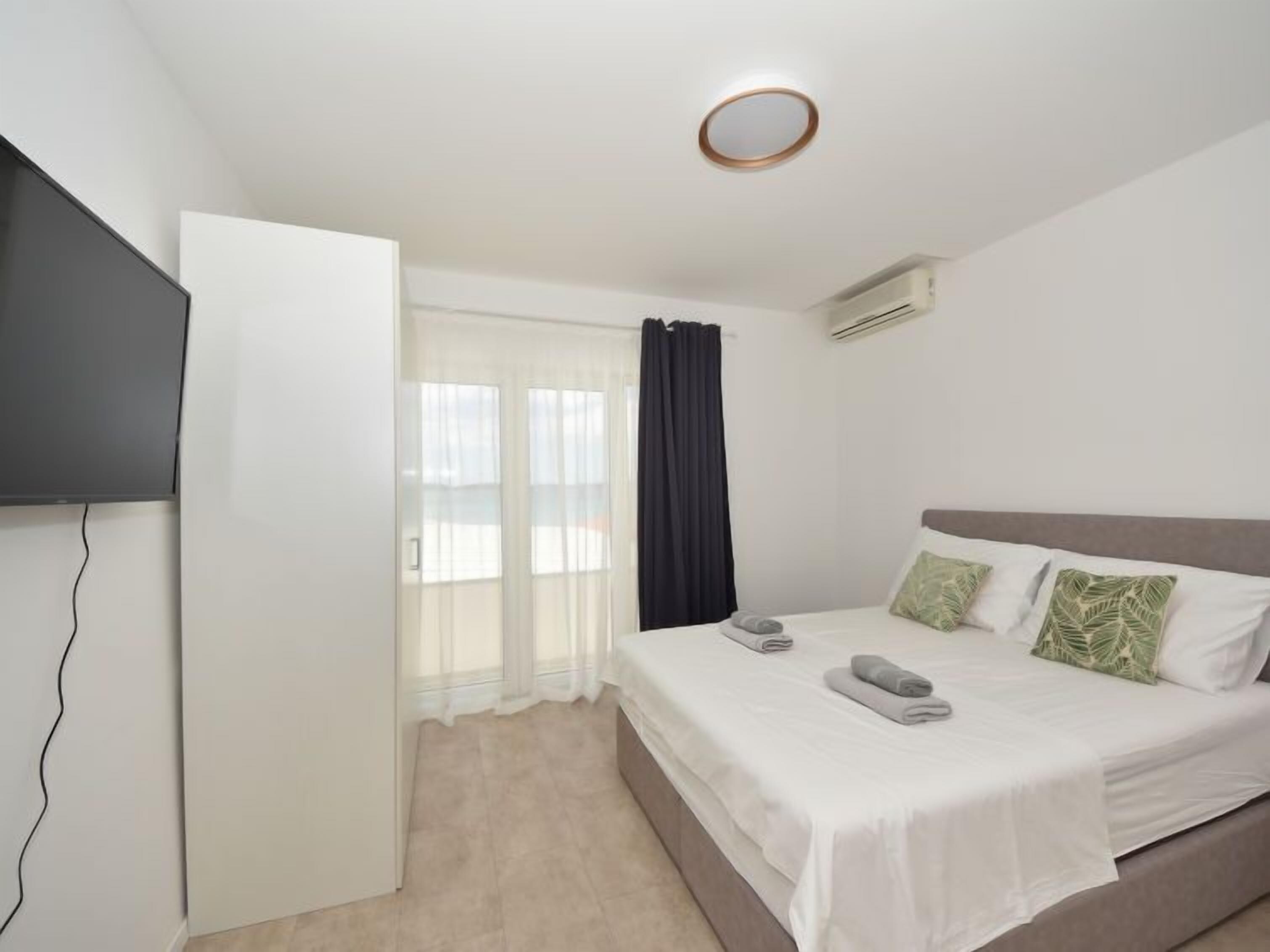A hotel room with a bed, a TV, a window with curtains, and an air conditioning unit.