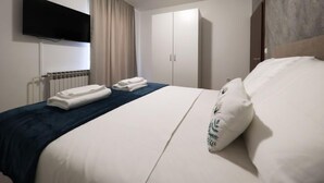 A hotel room with a bed, a flat-screen TV mounted on the wall, a wardrobe, and a radiator.