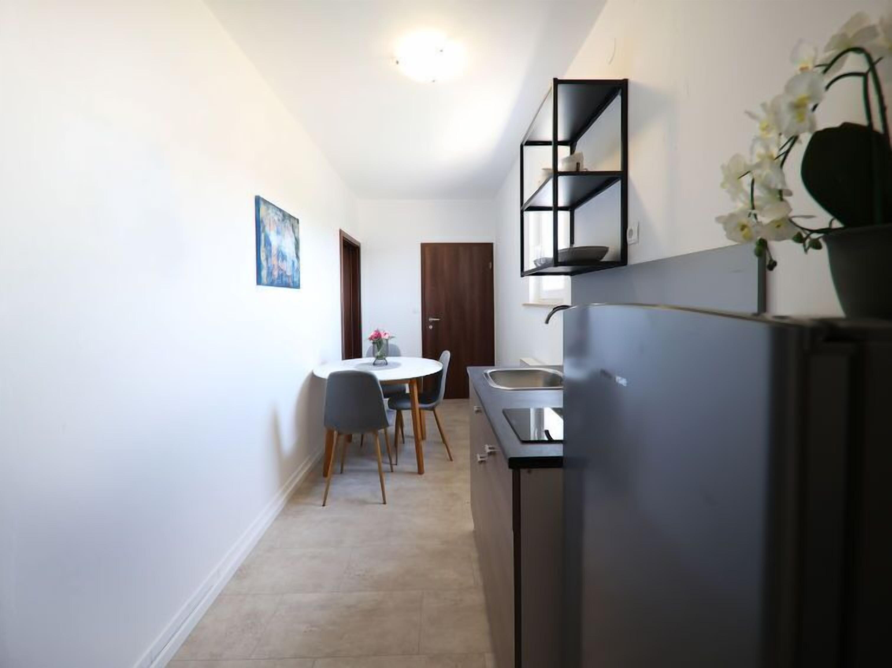 A compact kitchen with a refrigerator, sink, and a small dining table with chairs.