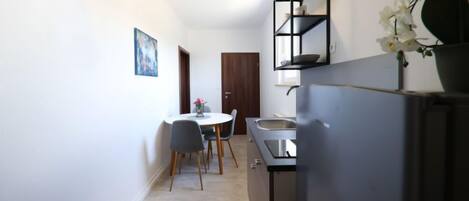 A compact kitchen with a refrigerator, sink, and a small dining table with chairs.