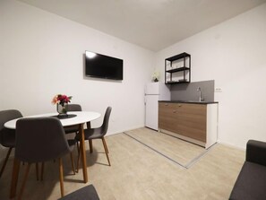 Eine kompakte Küche mit einem weißen Kühlschrank, einer schwarzen Regaleinheit und einem flachbildfernseher an der Wand.
