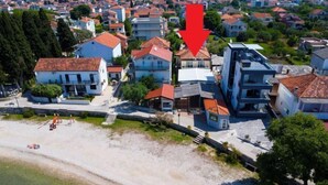 Ovenudblik over et kystnært boligområde med huse, en strand og en rød pil, der peger på en bestemt placering.