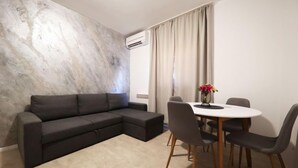 En moderne stue med en grå hjørnesofa, et rundt spisebord med fire stole og en væg med marmor.
