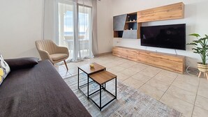 Uma sala de estar com sofá, poltrona, mesa de centro, televisão e uma planta.