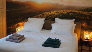 Een slaapkamer met een groot bed, witte lakens en uitzicht op een zonsondergang.