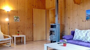 A cozy room with wooden walls, a sofa, a coffee table, a small table with a vase, and a fireplace. - Elsighornblick by Interhome (Kandergrund)