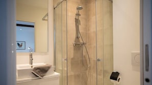 Un baño moderno con ducha acristalada, lavamanos blanco con una toalla y un espejo.