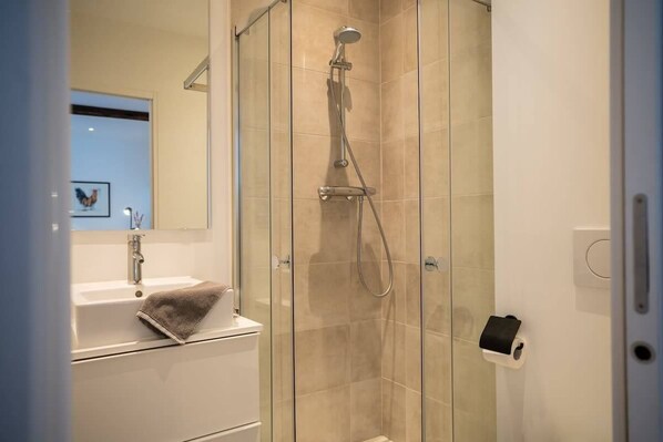 Une salle de bain moderne avec une douche à parois de verre, un lavabo blanc avec une serviette et un miroir.