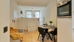 A compact living space with a kitchenette, a dining area with a table and chairs, and a sofa with a blanket.