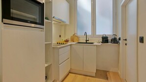 A compact kitchen with white cabinets, a built-in oven, a window, and a sink.