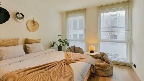 A bedroom with a bed, bedside tables, a lamp, and a window with blinds.