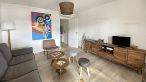 Una sala de estar moderna con un sofá gris, una mesa de centro de madera, un mueble para televisión y un cuadro abstracto de colores en la pared.