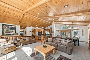 A spacious living area with wooden ceilings, a large sofa set, a dining table, and a kitchen in the background. - Hastings Hideaway Cabin (Kings Beach)