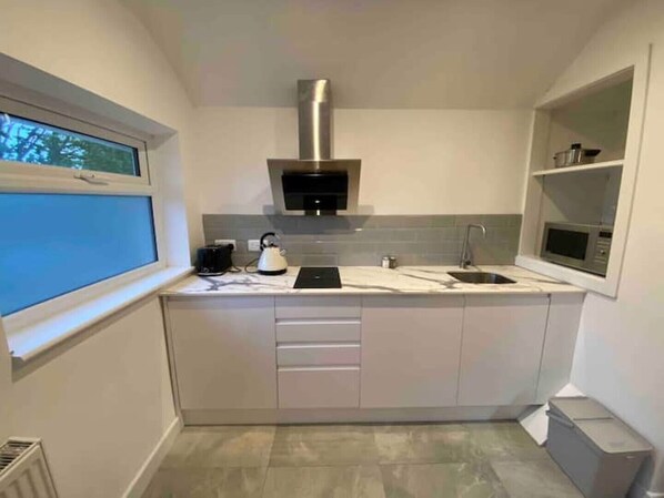 Efficient kitchen with stainless steel range hood, microwave, and kettle, plus a window for natural light and storage shelf.